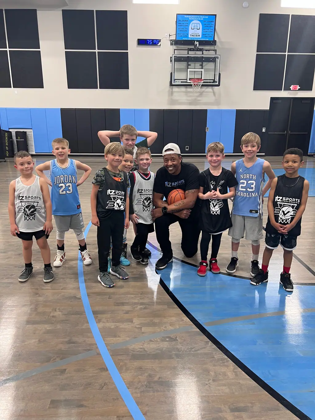A coach kneeling with a basketball, surrounded by a group of young players posing on the court
