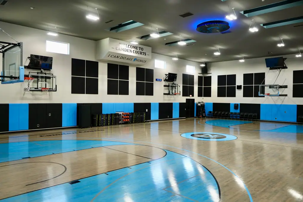 Full-court view of the gym with blue and black wall pads and wall-mounted side hoops