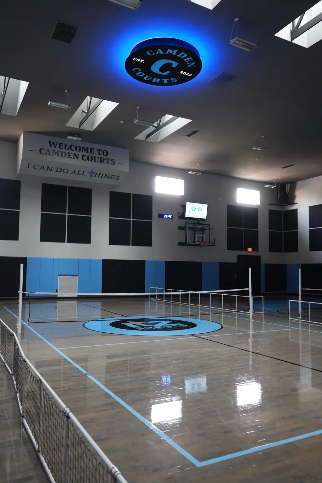 Tall view of the gym with pickleball nets set up on the court beneath a blue-lit ceiling sign