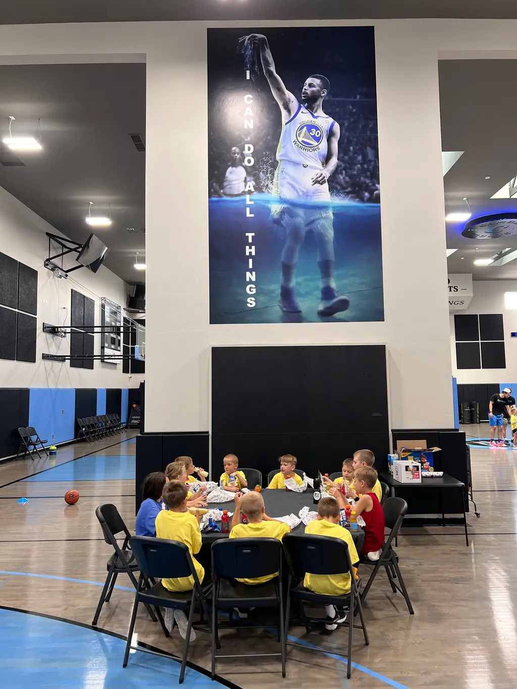 Kids eating together at a table on the gym floor beneath the wall mural