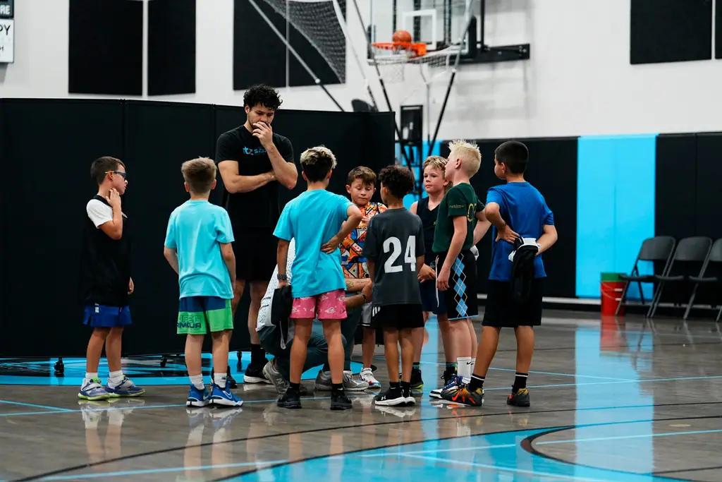 A coach speaking with a small group of basketball players on the blue court at SBC