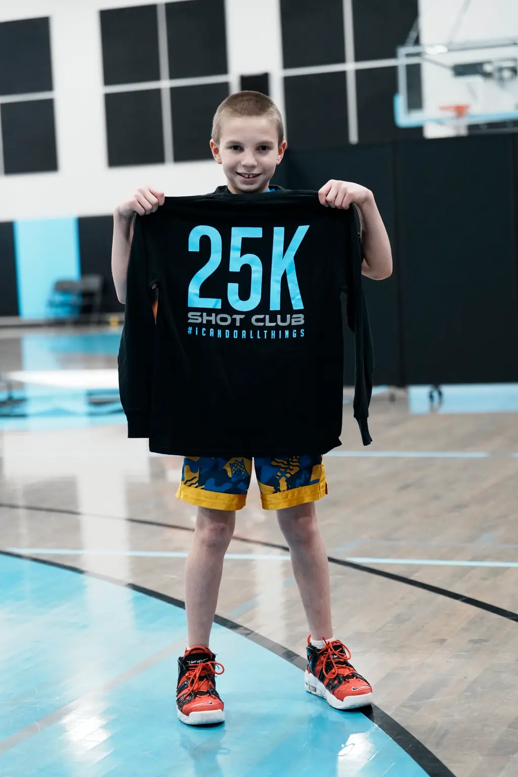 A young athlete holding a 25K Shot Club shirt