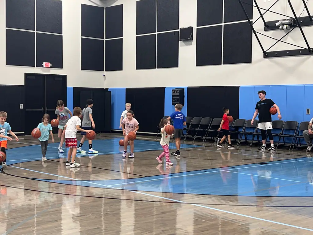 Young players dribbling across the court in a group drill while a coach watches